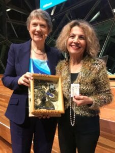 Two women smiling, one holding a framed artwork.